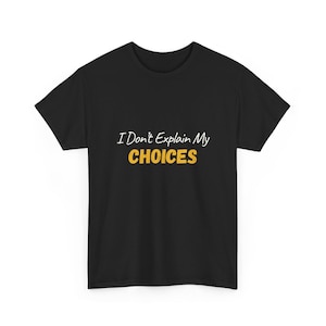 Puede incluir: Camiseta negra con la frase "I Don't Explain My CHOICES" en blanco y amarillo. La camiseta es de cuello redondo y parece estar hecha de un material suave. El texto está centrado en la parte delantera de la camiseta.