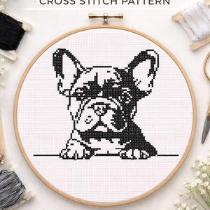 May include: A cross-stitch pattern of a French Bulldog in black and white, displayed in a wooden embroidery hoop. The text at the top reads "French Bulldog Cross Stitch Pattern". The image also includes the text "PDF Pattern", "Instant Download", and "Beginner Friendly".