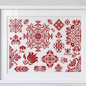 Puede incluir: Un muestrario de punto de cruz enmarcado que presenta una colección de intrincados patrones geométricos y florales rojos sobre un fondo de tela blanca. El diseño incluye varios motivos simétricos, como diamantes, flores estilizadas y bordes ornamentados.