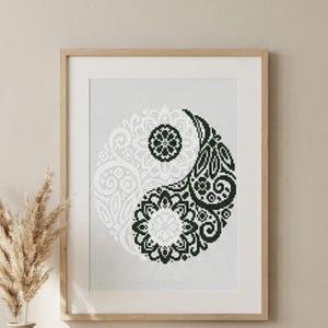 Puede incluir: Obra de arte en punto de cruz enmarcada con el símbolo del Yin y Yang. El diseño presenta un patrón detallado en blanco y negro. La obra de arte se presenta en un marco de madera. El símbolo del Yin y Yang es una representación clásica del equilibrio y la armonía.