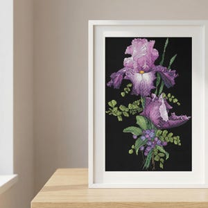 Pu&ograve; includere: Una stampa artistica incorniciata con fiori di iris viola e foglie verdi su sfondo nero. L'opera d'arte &egrave; in una cornice bianca, posizionata su una superficie di legno vicino a una finestra.