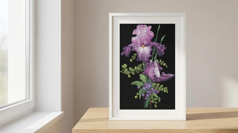 Pu&ograve; includere: Una stampa artistica incorniciata con fiori di iris viola e foglie verdi su sfondo nero. L'opera d'arte &egrave; in una cornice bianca, posizionata su una superficie di legno vicino a una finestra.