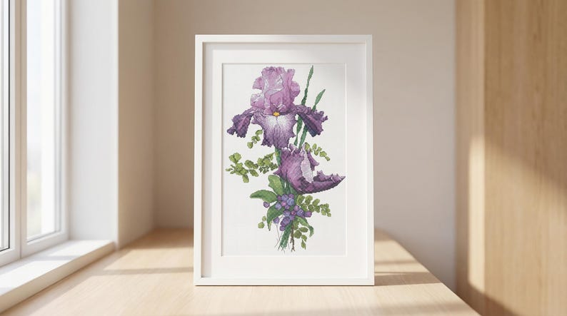 Pu&ograve; includere: Una stampa incorniciata con un'illustrazione ad acquerello di fiori di iris viola. L'opera presenta petali dettagliati, fogliame verde e piccole bacche viola. La cornice bianca &egrave; esposta su una superficie di legno vicino a una finestra.