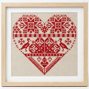 May include: Framed cross-stitch art featuring a large red heart design with geometric patterns and two bird figures. The artwork is set against a neutral background and framed in a light wood frame, suitable for home decor.