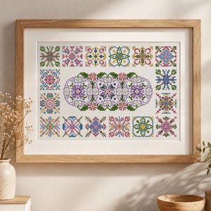 Può includere: Un ricamo a punto croce incorniciato con un motivo ovale centrale composto da tre grappoli floreali nelle tonalità del viola, rosa e verde, circondato da un bordo di sedici singoli motivi geometrici quadrati in vari colori.