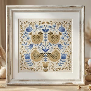 May include: A framed cross-stitch with a symmetrical design of birds and floral elements in blue, tan, and cream. A plush bunny and a nest of pastel Easter eggs are in the foreground, creating a spring theme.