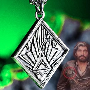 May include: Silver-colored pendant with a geometric design, hanging from a silver chain. The pendant is diamond-shaped with an engraved pattern featuring lines and shapes. The background is a vibrant green.