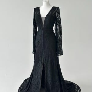 May include: A black lace gown with a plunging V-neckline and long sleeves. Black lace mermaid wedding dress long sleeves 
deep V neckline on mannequin, floor
