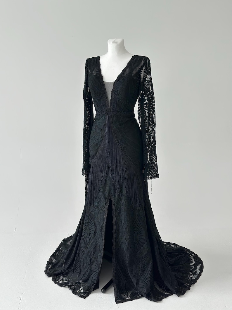 May include: A black lace gown with a plunging V-neckline and long sleeves. Black lace mermaid wedding dress long sleeves 
deep V neckline on mannequin, floor