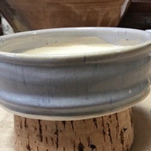 May include: A light blue ceramic bowl with a wide rim, filled with a light-colored liquid. The bowl sits on a cork base, with a small panda figurine to the right. The bowl has a textured, glazed finish.