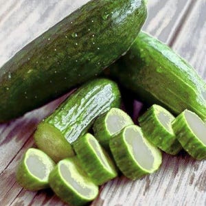 Può includere: Primo piano di cetrioli verdi freschi, interi e a fette, su una superficie di legno. I cetrioli hanno una buccia verde scuro e un interno verde chiaro. Le fette rivelano una consistenza croccante.