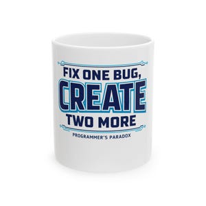 May include: White ceramic coffee mug with the text "FIX ONE BUG, CREATE TWO MORE" in blue and white. The phrase "PROGRAMMER'S PARADOX" is printed below the main text. The mug is a standard size and shape.