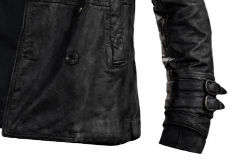 May include: Black leather jacket with a textured finish. The jacket features a double-breasted design with a single button closure and a small pocket. The sleeve has a cuff with two buckles. The jacket appears to be worn and distressed.