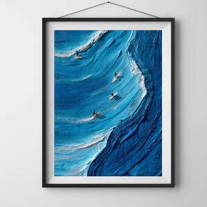 May include: A framed art print depicting surfers riding a large blue wave. The artwork features a textured, almost 3D effect, with white foam cresting the wave. The surfers are small figures on surfboards.