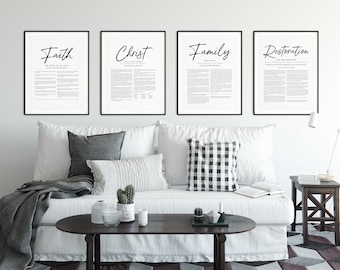 May include: Four black framed prints with white backgrounds and black text. The prints are hanging on a white wall above a white couch with gray and black pillows. The prints feature the words "Faith", "Christ", "Family", and "Restoration".