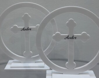 May include: Two white decorative crosses with the name "Andre" inscribed on them. Each cross is set within a circular frame and mounted on a rectangular base. The design is simple and elegant.