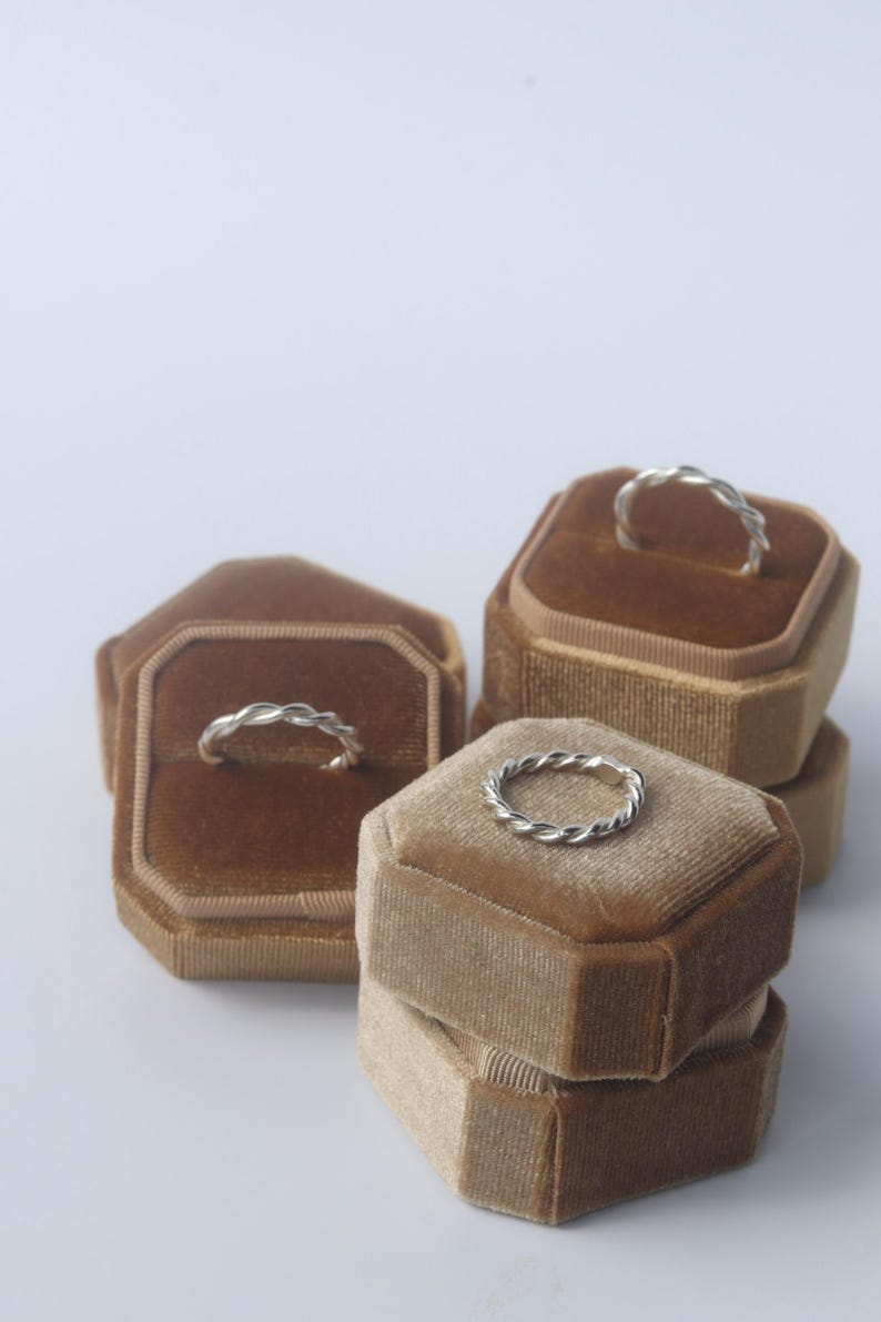 K&ouml;nnte beinhalten: Drei silberne Ringe mit gedrehter Seilstruktur, die jeweils auf einer achteckigen Ringbox aus braunem Samt pr&auml;sentiert werden. Die Ringe verf&uuml;gen &uuml;ber ein durchgehendes geflochtenes Metalldesign mit polierter Oberfl&auml;che und runder Form.