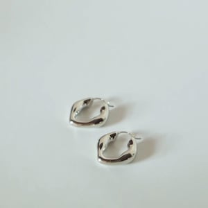 May include: A pair of silver-toned hoop earrings with an irregular, organic, and wavy shape. The earrings feature a polished, reflective metallic surface and a hinged post closure mechanism, showcasing a distinct, non-circular, fluid design.