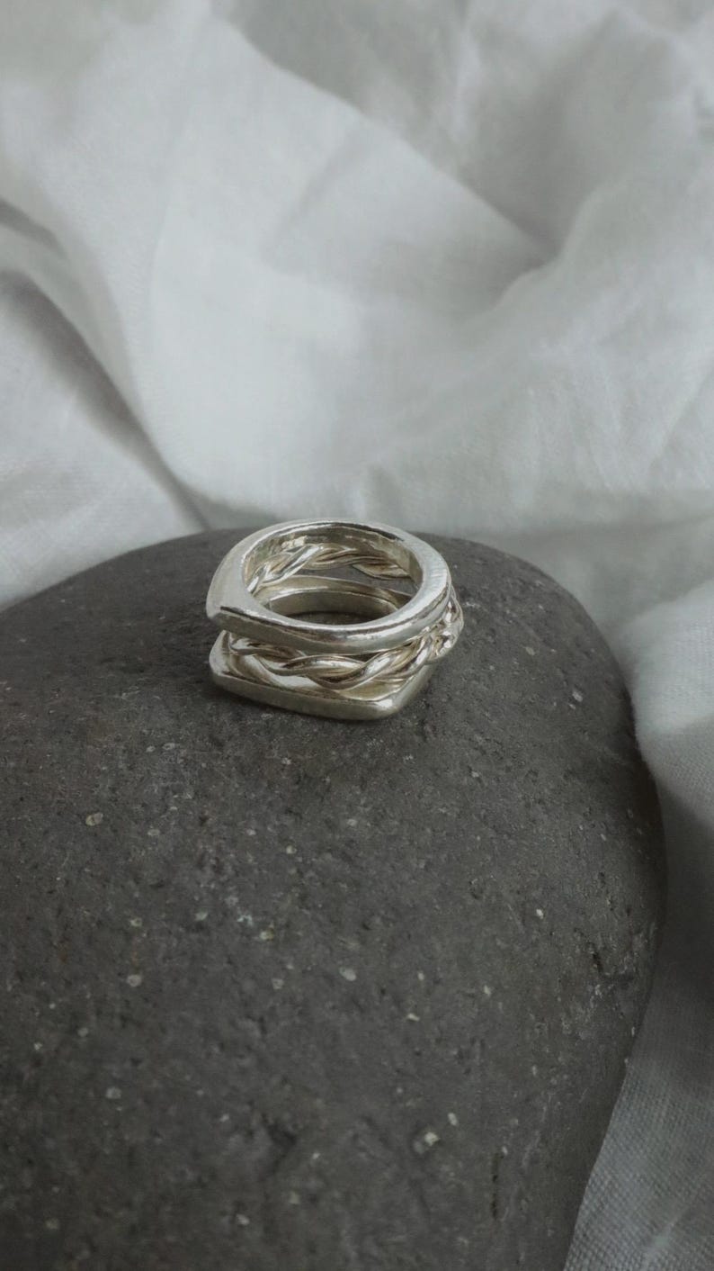 K&ouml;nnte beinhalten: Ein silberner Ring mit einem gestapelten Design aus zwei verschiedenen B&auml;ndern. Das obere Band besteht aus einem glatten, abgerundeten Silberdraht, w&auml;hrend das untere Band aus einem gedrehten, geflochtenen Silberdraht gefertigt ist. Polierte Oberfl&auml;che.