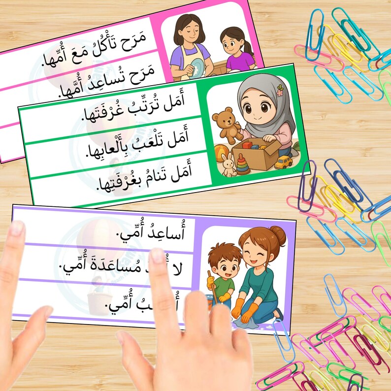 May include: Educational flashcards with Arabic text and colorful illustrations. The cards feature images of children and adults performing daily activities. A collection of colorful paper clips are scattered around the cards.