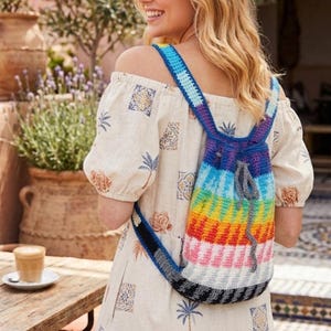 Peut inclure: Un sac à dos crocheté à la main aux couleurs de l'arc-en-ciel. Le sac est doté d'une fermeture à cordon et de bretelles réglables. Le motif du sac à dos comprend des rayures bleues, violettes, vertes, jaunes, oranges, roses, blanches et noires. Les bretelles sont bleues et noires.