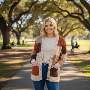 Peut inclure: Un cardigan à patchwork dans les tons beige, marron et rouille. Le pull ouvert sur le devant a une fermeture boutonnée et deux poches avant. La femme porte le cardigan avec un haut crème et un jean bleu.