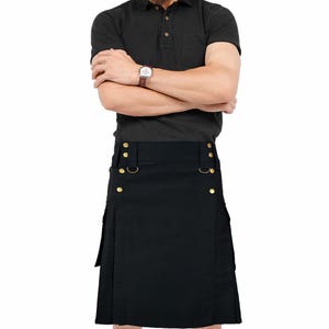 Op de afbeelding: Zwarte kilt met goudkleurige knopen en metalen ringen. De kilt heeft een geplooid ontwerp en een zijzak. Het kledingstuk is gemaakt van een stevig materiaal, geschikt voor zowel functionaliteit als mode.