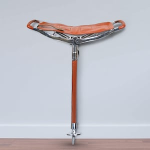 May include: A brown leather folding seat attached to a silver metal frame with a long brown leather-wrapped metal pole. The pole has a silver metal base with a pointed tip.