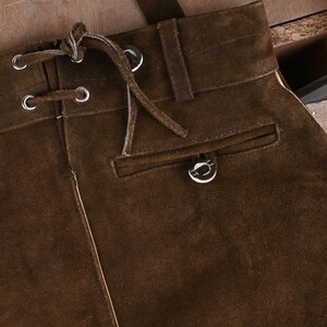 May include: A dark brown suede skirt featuring a high waistband with belt loops, a front lace-up closure with silver-toned metal grommets and matching suede laces, and a single horizontal welt pocket with a silver-toned metal button detail.
