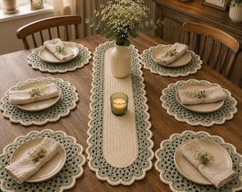 May include: A dining table set featuring a long, oval, cream and sage green crocheted table runner and six matching round crocheted placemats. Each placemat holds a ceramic plate, a folded beige napkin, and a small sprig of baby's breath.