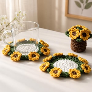 May include: Crocheted sunflower coasters with yellow petals and brown centers, surrounding a white center. A clear glass mug sits on one coaster. A small crocheted sunflower arrangement is also present.