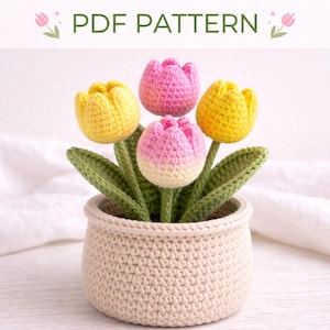 以下が含まれることがあります： ベージュの鉢に4つのチューリップをあしらったかぎ針編みのフラワーアレンジメント。 黄色とピンクのチューリップが2つずつ、緑の葉とともに飾られています。 上部には「PDF PATTERN」の文字。 鉢は明るいベージュ色です。
