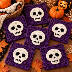 May include: Five square crochet coasters in deep purple yarn, each featuring a centred white skull motif with black yarn detailing for the eye sockets, nose, and teeth. The coasters are arranged in a cluster on a wooden surface.