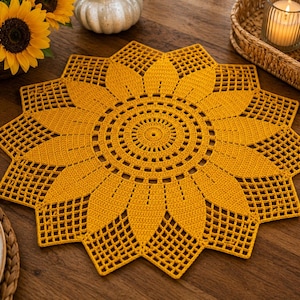 May include: A circular crochet doily in a vibrant golden yellow color, featuring a detailed sunflower pattern with a solid center, radiating petals, and an intricate openwork lattice border that creates a star-like shape with pointed edges.