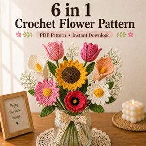 May include: A handmade crochet flower arrangement in a glass vase, featuring tulips, a sunflower, daisies, and a poppy. The vase is tied with a ribbon. A small framed sign reads "Enjoy the little things".