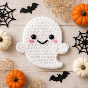 May include: A white crocheted ghost applique with black safety eyes, a stitched black mouth, and small pink cheeks. The ghost is surrounded by orange and white pumpkins, black felt spider webs, black bat silhouettes, and dried baby's breath flowers.
