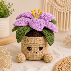 Puede incluir: Una maceta de ganchillo con una cara sonriente, una maceta marrón claro y una flor lavanda. La flor tiene hojas verdes y estambres amarillos. La maceta tiene pequeños pies redondos. El diseño general es caprichoso y hecho a mano.