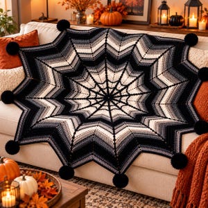 May include: A large, circular crochet blanket featuring a spiderweb pattern in a gradient of black, gray, and white yarn. The edges of the blanket are pointed and finished with black yarn pom-poms at each of the eight outer corners.