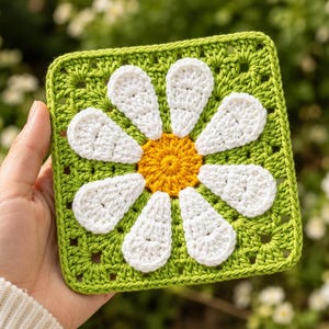 May include: A square crochet granny square featuring a central yellow circle surrounded by eight white petals, all set against a bright green background. The piece is crafted with a textured yarn stitch pattern, creating a floral motif in a square shape.