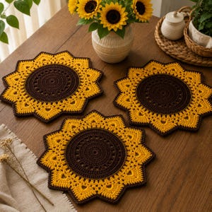Könnte beinhalten: Drei kreisförmige Häkeldeckchen, die wie Sonnenblumen gestaltet sind, mit einer dunkelbraunen Mitte und leuchtend gelben Blütenblättern, die einen spitzen, sternförmigen Rand bilden. Diese handgefertigten Textilmatten liegen auf einer Holzoberfläche.