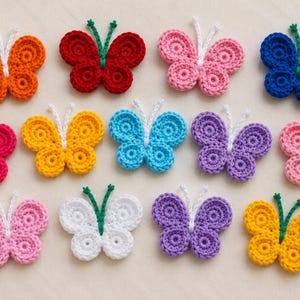 May include: A collection of thirteen crocheted butterfly appliques in various colors including orange, red, pink, blue, yellow, purple, and white. Each butterfly features a central body with two antennae and four rounded, textured wings.