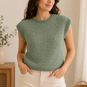 May include: A sage green sleeveless knit sweater vest featuring a textured ribbed pattern, a round crew neckline, and wide ribbed armholes. The garment has a straight hemline with a ribbed finish, providing a structured and consistent knit texture.