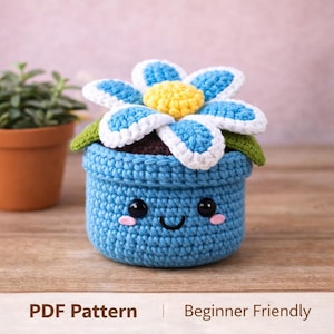 Puede incluir: Una maceta azul de ganchillo con una cara sonriente, que sostiene una flor grande con pétalos azules y blancos y un centro amarillo. El texto "PDF Pattern | Beginner Friendly" está en la parte inferior.