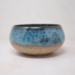 Peut inclure: Un bol en céramique fait à la main de forme arrondie. La partie supérieure est émaillée dans des tons de bleu, passant à une base beige texturée. L'intérieur du bol est bleu foncé. Ce bol décoratif convient au service ou à l'exposition.