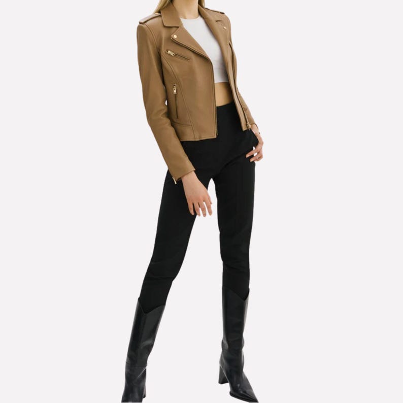May include: A tan leather jacket with a classic biker style, featuring a notched collar, asymmetrical zipper, and multiple pockets. The jacket is paired with black pants and knee-high black boots. The outfit is completed with a white top.