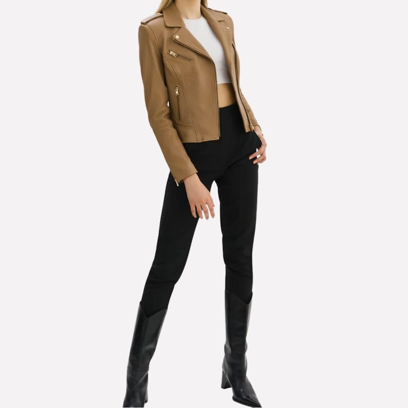 May include: A tan leather jacket with a classic biker style, featuring a notched collar, asymmetrical zipper, and multiple pockets. The jacket is paired with black pants and knee-high black boots. The outfit is completed with a white top.