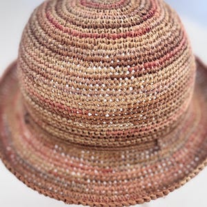 May include: A woven straw hat with a wide brim and a brown and pink color scheme. The hat is made of a natural material and has a crocheted texture.