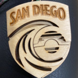 May include: A wooden ornament with a wave design and the text "SAN DIEGO" in a brown font.