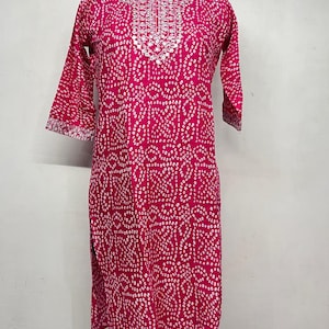 Puede incluir: Una túnica magenta con un estampado de puntos blancos y mangas tres cuartos. El escote y los puños de las mangas presentan intrincados bordados blancos. El vestido se exhibe en un maniquí.