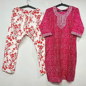 Puede incluir: Un conjunto de dos piezas con un conjunto de pijama con estampado floral blanco y una túnica magenta. El pantalón de pijama tiene un estampado floral rojo. La túnica tiene un estampado de puntos blancos y bordados plateados.
